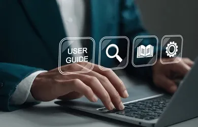 A person typing on a laptop, with icons for a user guide, search, a book and settings floating above the keyboard.